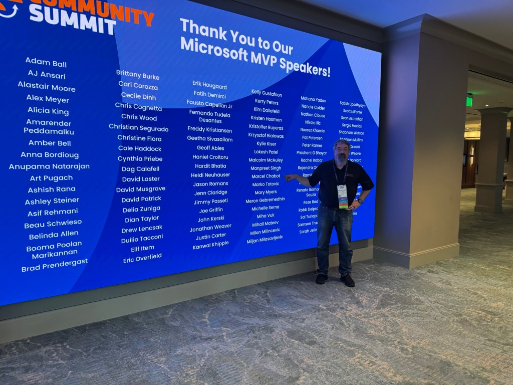 A man stands next to a large display screen at a conference, thanking Microsoft MVP speakers. The screen features a list of names in a blue background with 'Thank You to Our Microsoft MVP Speakers!' prominently displayed.